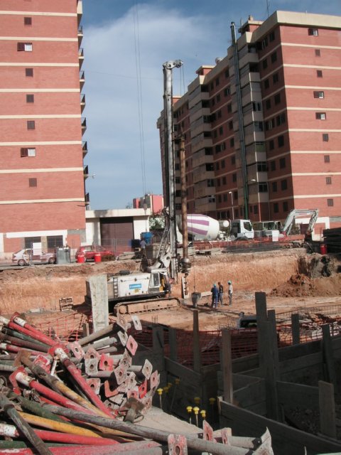 Equipo de pilotaje dentro de una excavación con operarios y acopios próximos.
