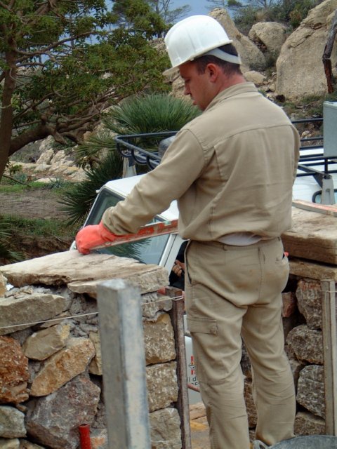 Trabajador con casco y guantes comprobando un muro con un nivel.